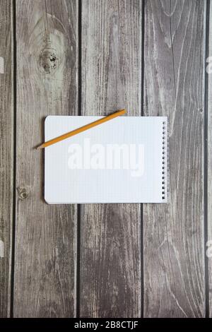 Notepad with a blank white sheet in a checker paper with simple graphite pencil lies on the background of wooden boards Stock Photo