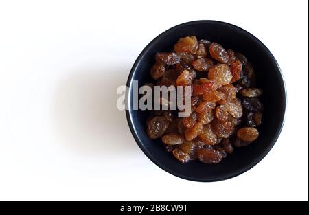 Concept of healthy food. A black bowl with sweet dried raisins isolated on white background. Top view. Stock Photo
