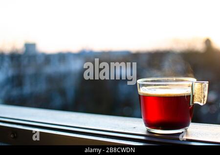 Glass cup of hot tea, hot beverage with city blur background. Red beverage. Coffee. Stock Photo