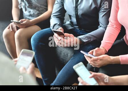 Group of millennial business people using mobile phones and sitting on couch. Networking and teamwork. Working on project with wireless technology. Stock Photo