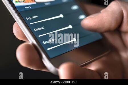 Photo edit with mobile phone and smart app. Man adjusting sliders. Image editing, manipulation, improvement or enhancement with smartphone. Stock Photo