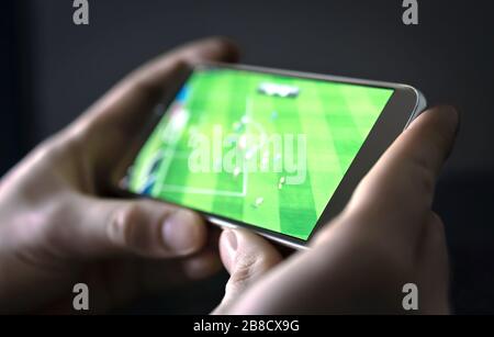 Watching football and sport stream with mobile phone. Man streaming soccer game live, video replay or highlights online with smart device. Stock Photo