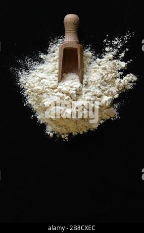Wheat flour with a wooden scoop isolated on dark background. Top view. Stock Photo
