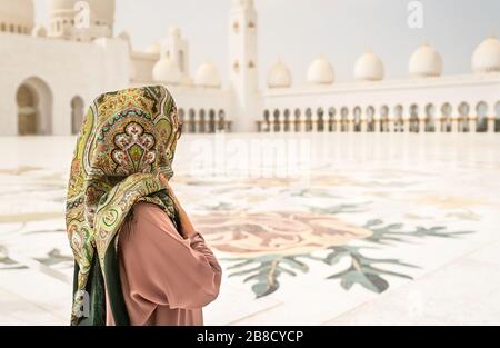 Back view of Woman in The Sheikh Zayed Grand Mosque. Traditional Muslim building in the United Arab Emirates. Female visitor wearing headscarf. Stock Photo