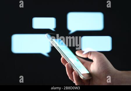 Text messages in cellphone screen with abstract hologram speech bubbles. Instant messaging app. Texting, group chat, sexting or sms concept. Stock Photo