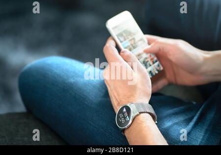 Wireless connection between smart watch and mobile phone. Man using wearable gadget and digital app. Person wearing future wristwatch in hand. Stock Photo