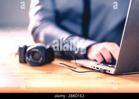 Camera connected to laptop with usb cable. Man editing photos with computer software. Photographer transfer files to computer from DSLR. Stock Photo