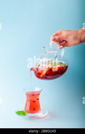 Female hand pouring fruit tea from teapot to cup Stock Photo