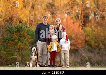 A portrait of a happy young family with mother and father and their 3 children standing outside in the woods with their pet rescued dog on a beautiful Stock Photo