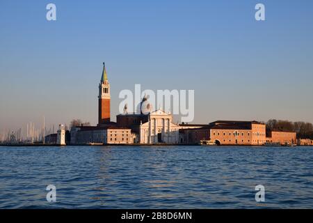 From de water view on the island of Saint Giorgio Maggiore during golden hour with dome and Campanile clearly visible against a blue sky Stock Photo