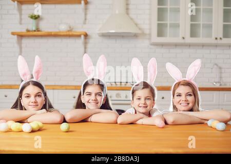 Happy easter. Mother and daughters with rabbit ears decorate Easter eggs at a table in kitchen. Stock Photo