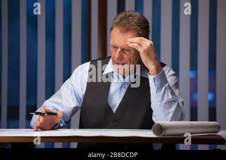 Mature businessman, architect or engineer sitting at a desk in an office late at night Stock Photo