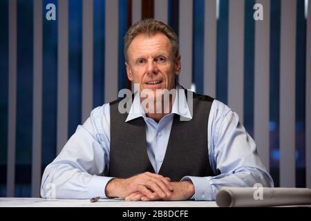 Mature businessman sitting at a desk in an office in the evening smiling at the camera Stock Photo