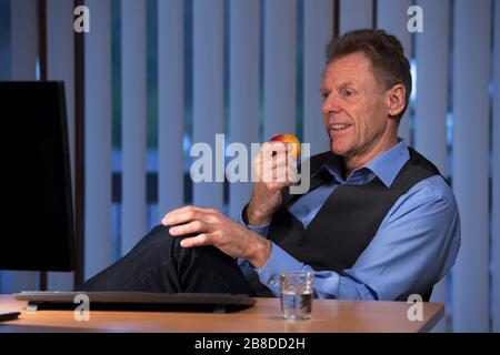 Senior businessman eating an apple at his desk with monitor and a glass of water Stock Photo