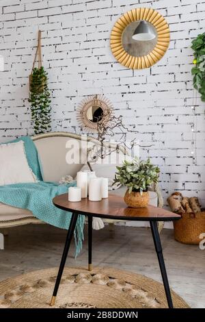 Beige and texture pillows on beige sofa, mint blanket.Small table with candles. Stylish scandinavian interior of living room with sofa, pillows Stock Photo