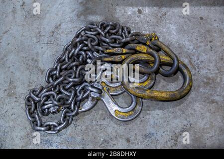 old industrial crane chain lays on concrete floor with rings and hooks Stock Photo