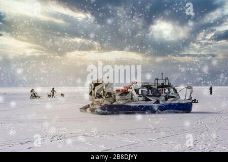 People travel, dogsledding on the ice of frozen Baikal Lake in a safe and comfortable Hivus hovercraft. Stock Photo