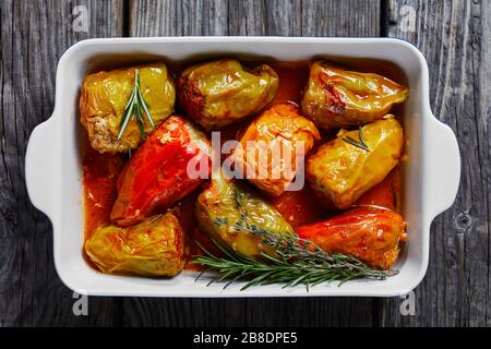 Stuffed bell peppers with rice and minced meat: beef and pork with tomato sauce, rosemary and thyme on top baked on a baking dish, on a wooden backgro Stock Photo