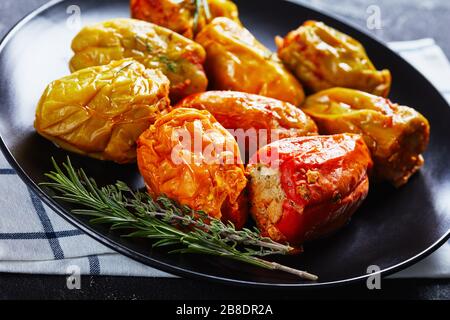Bell peppers stuffed with rice, ground beef, and pork baked in tomato sauce, rosemary and thyme on a black plate on a dark concrete background, close- Stock Photo