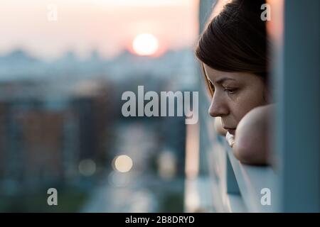 Young sad woman looking outside through balcony of an apartment building Stock Photo