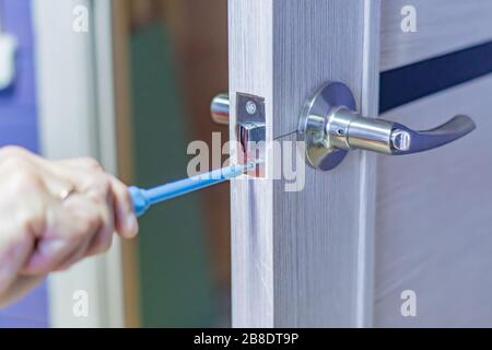 man repairing the doorknob with screwdriver. worker's hand installing new door locker Stock Photo