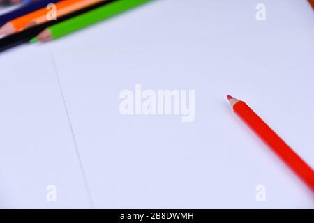 Red pencil on a white sheet with blurry multicolored pencils in the background Stock Photo