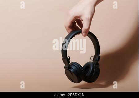 Hand hold black wireless headphones isolated on beige color background Stock Photo