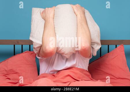 Young caucasian man covering face with a pillow being stress. Studio shot Stock Photo
