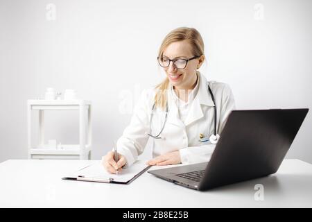 Female doctor sitting at table and writing in clipboard Stock Photo