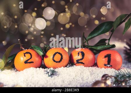 New Year 2021 is Coming Concept. Numbers written in Black Ink on the Oranges that are laying in the Basket with Pine Sticks and Xmas Lights on the Background Stock Photo
