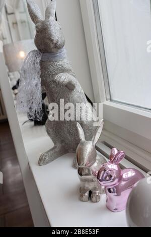 Silver easter bunnies sitting on sideboard. High angle view of bunnies sitting in front of white bright window. Metal composition for Holiday concept. Stock Photo