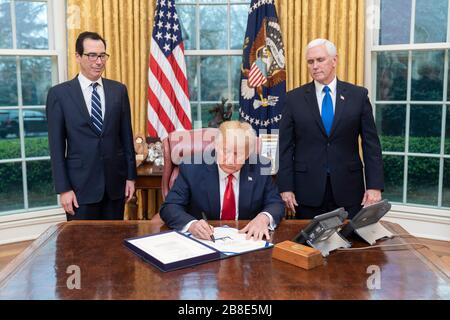 U.S President Donald Trump joined by Vice President Mike Pence and Secretary of the Treasury Steven Mnuchin signs H.R. 6201, the Families First Coronavirus Response Act, in the Oval Office of the White House March 18, 2020 in Washington, DC. Stock Photo