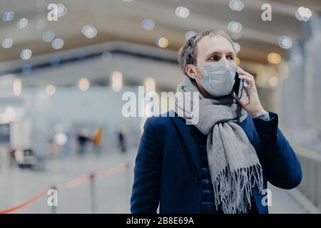 Health, communication and epidemy concept. Serious man wears protective medical mask, cares about safety not to catch coronavirus, walks in shopping m Stock Photo