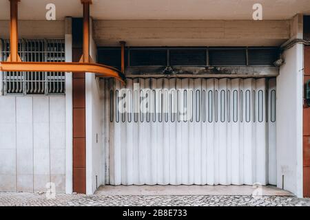Front wide-angle view of a modern vertical folding white gate in a residential building or gates of an entrance to a warehouse of some mall, with a me Stock Photo