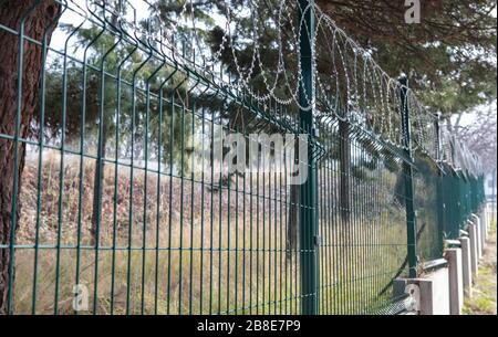 Steel grating fence of field,Metal fence wire. Coiled razor wire with its sharp steel barbs on top of a wire mesh perimeter fence ensuring safety and Stock Photo