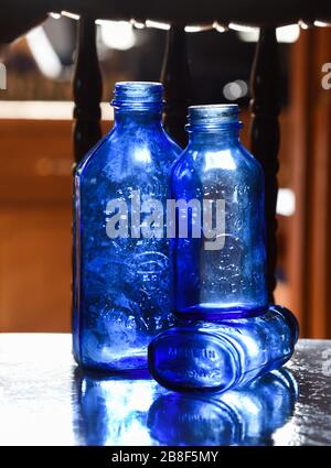 Three empty milk of magnesia blue bottles sitting on reflective shelf. Made in America embossed on bottom Stock Photo