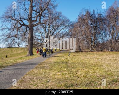 Tarrytown, NY - 21 March 2020: On the first day of spring, New Yorkers hike in Rockefeller State Park as cases of coronavirus top 10,300 in the state. Although NY Governor Andrew Cuomo has ordered all but workers in essential services such as healthcare and groceries to work from home, and to stay home except when necessary, he has also encouraged people to exercise outdoors, noting this means hiking, running, not playing basketball with groups of people. With fewer vehicles on the road, the sky, and therefore the Hudson River, are a beautiful blue. Stock Photo