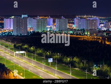 Multiple white marble residential buildings. Empty Archabil highway in foreground with ornamented lamp posts in exotic city of Ashgabat, Turkmenistan. Stock Photo