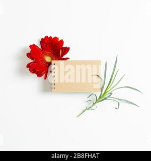 Empty notebook with red gerbera flower on white background. Floral composition, flat lay, top view, copy space Stock Photo
