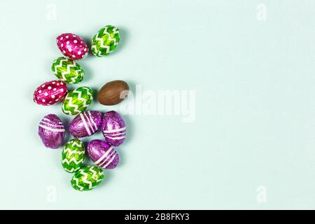 Colorful chocolate easter eggs on blue background. Small Chocolate eggs in a foil. Traditional Easter sweet. Copy Space Stock Photo