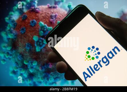 In this photo illustration the  Irish-domiciled pharmaceutical company  Allergan logo seen displayed on a smartphone with a computer model of the COVID-19 coronavirus on the background. Stock Photo