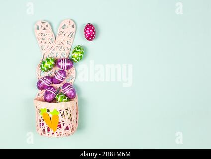 Easter basket full of Colorful chocolate easter eggs on blue background. Small Chocolate eggs in a foil. Traditional Easter sweet. Copy Space Stock Photo