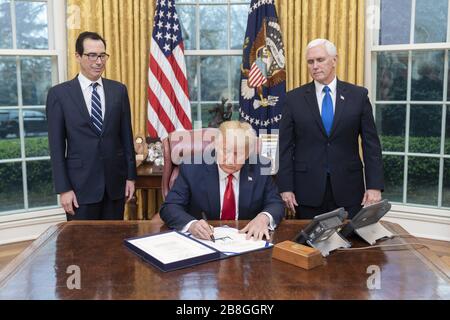 Washington, United States Of America. 18th Mar, 2020. President Donald J. Trump, joined by Vice President Mike Pence and Treasury Secretary Steven Mnuchin, signs H.R. 6201, the Families First Coronavirus Response Act Wednesday, March 18, 2020, in the Oval Office of the White House People: President Donald Trump Credit: Storms Media Group/Alamy Live News Stock Photo