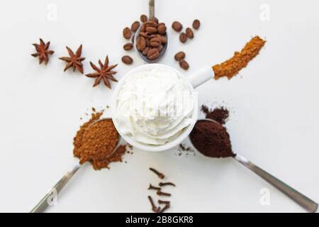 Cup of cappuccino with cinnamon and spilled out coffee beans. A cup of coffee with whipped cream on a background of different coffee and spices. Stock Photo