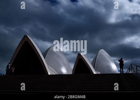 Sydney Opera House - Tourists silhouetted against the drama of the white sails and storm cloud sky at the top of the stairs on the upper podium. Stock Photo