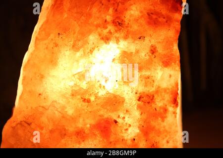 Himalayan salt lamp on wooden table illuminated in a darkend room Stock Photo