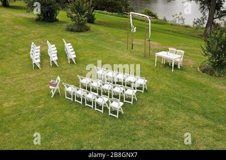 White chairs on a green lawn, ladders form a bridal arch, seating arrangement an outdoor wedding, on a grassy riverbank in Western Sydney, Australia Stock Photo