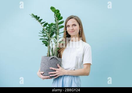 Happy woman standing with a plant in a wicker pot, she's holding in her hands Stock Photo
