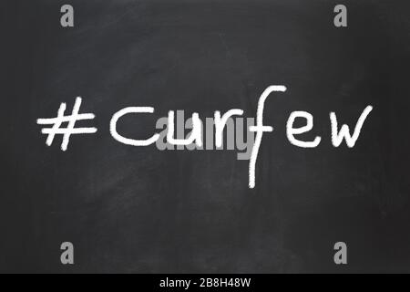 hashtag curfew as handwritten text on chalkboard - social distancing measure to control infection during corona virus pandemic Stock Photo