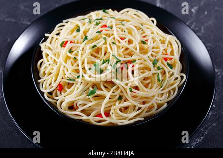 close-up of Pasta Aglio, Olio e Peperoncino, italian spaghetti with garlic, chili pepper and olive oil in a black bowl Stock Photo